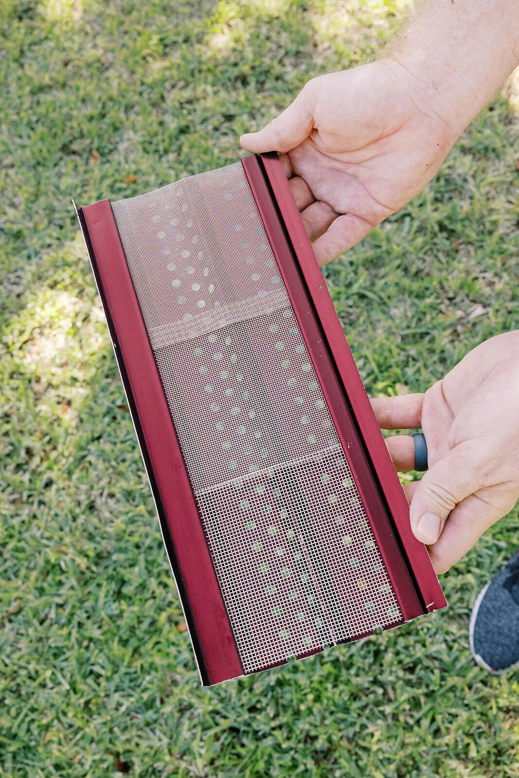 Red perforated mesh gutter guard held over lawn, Sanford FL